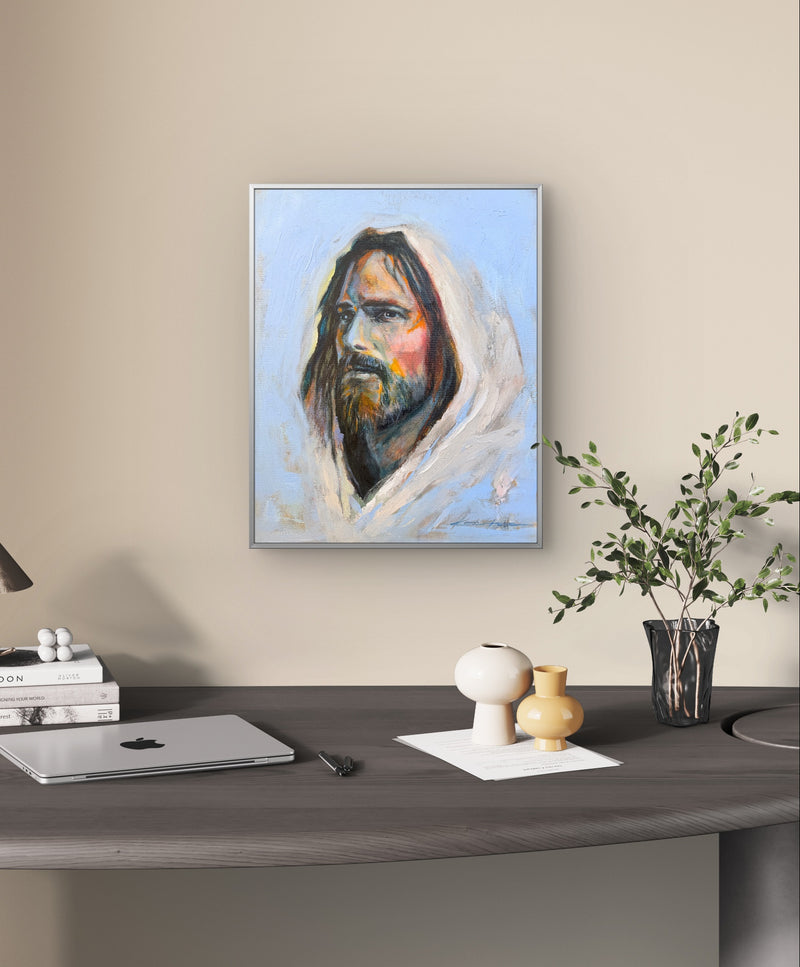 Framed Original Oil Painting, a portrait of Jesus with big brushstrokes and thick paint, a lot of texture and vibrant colors hanging over a desk in an office with a plant to the bottom right. 
